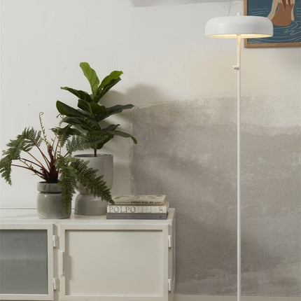 Lampadaire Porto fer blanc posé près d'un bahut et de plantes vertes, décor minimaliste et naturel.