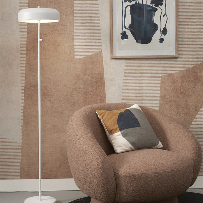 Lampadaire Porto fer blanc à côté d'un fauteuil beige, ambiance nordique épurée dans un salon lumineux.