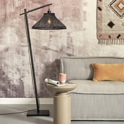 Lampadaire Tahiti en bambou tressé noir, bras déporté au-dessus d'un canapé dans un salon cosy