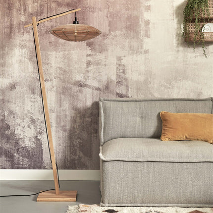 Lampadaire Tanami en bambou naturel avec abat-jour disque en rotin tressé, posé près d'un canapé dans un salon