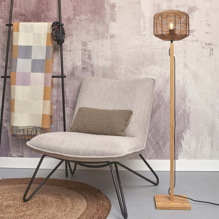 Lampadaire Tanami allumé à côté d'un fauteuil, abat-jour en rotin tressé et pied en bambou clair