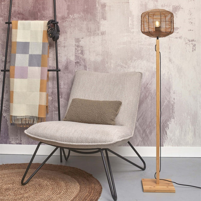 Lampadaire Tanami allumé à côté d'un fauteuil, abat-jour en rotin tressé et pied en bambou clair
