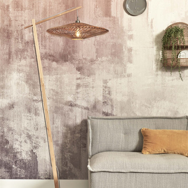 Lampadaire Zanzibar en bambou et rotin tressé installé dans un salon aux tons roses, près d'un canapé gris et d'un coussin moutarde.