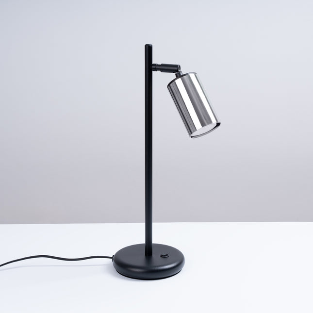 Lampe à poser Acier Luxe, tige noire et tête cylindrique chrome orientée, vue de trois quarts sur fond blanc.
