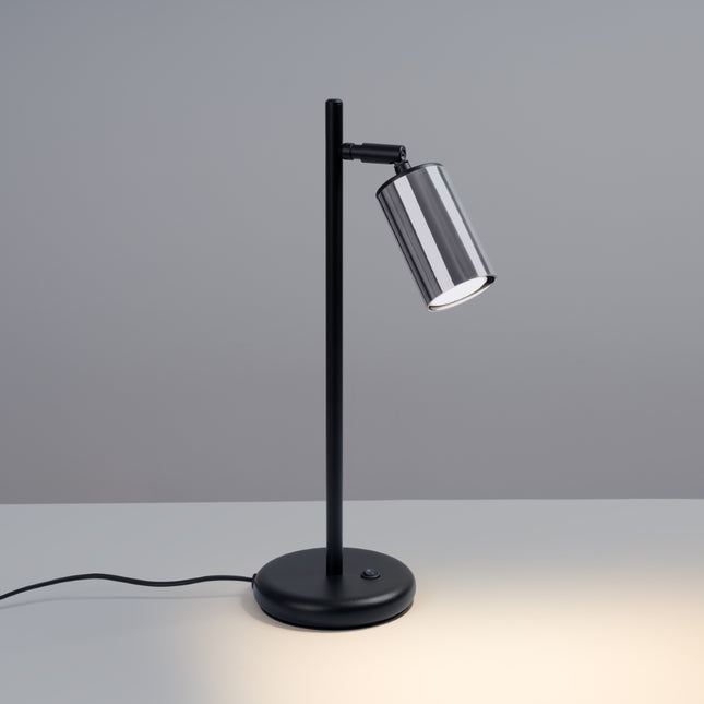 Lampe à poser Acier Luxe allumée, tête chrome orientable diffusant une lumière chaude et ciblée.