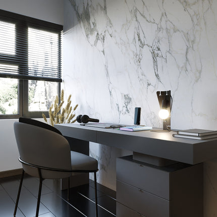 Lampe de bureau Arby en acier noir posée sur un bureau contemporain devant un mur en marbre