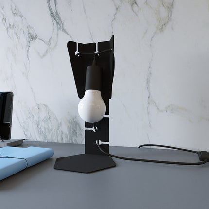Lampe à poser Arby en acier noir avec ampoule opale allumée, posée sur un plan de travail gris