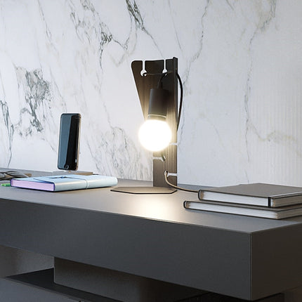 Lampe à poser Arby en acier noir allumée sur un bureau, ambiance de travail feutrée