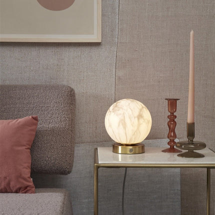 Lampe à poser Carrara globe en verre effet marbre blanc et base dorée sur une table basse