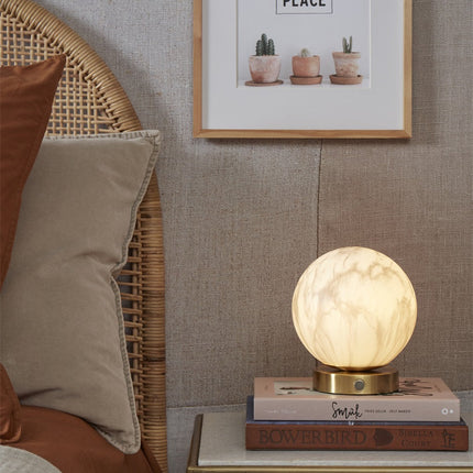 Lampe à poser Carrara globe marbre et or posée sur une table de chevet
