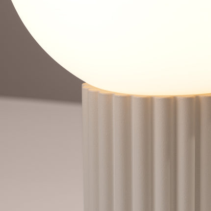 Détail des cannelures verticales du socle en aluminium beige sous le globe en verre opalin