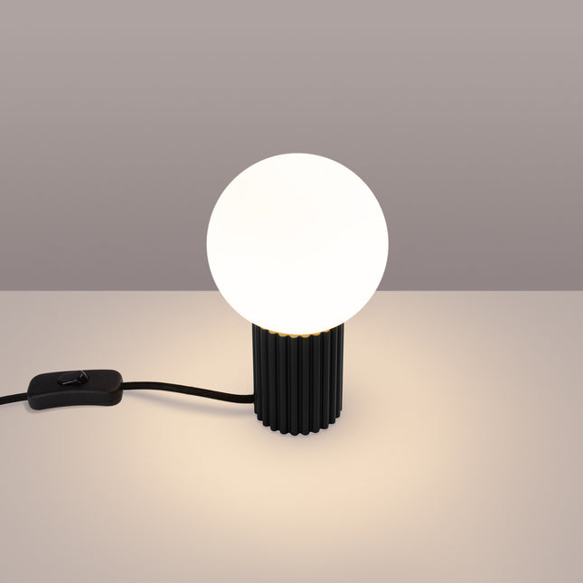 Lampe à poser Halo noire allumée, lumière chaude diffusée par le globe en verre opalin