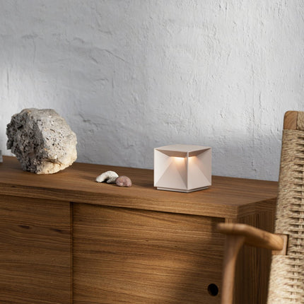 Lampe Nutalis allumée sur un meuble en bois, entourée de pierres décoratives, lumière chaude douce.