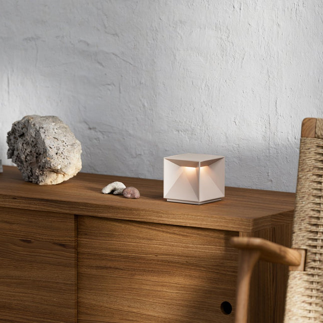 Lampe Nutalis allumée sur un meuble en bois, entourée de pierres décoratives, lumière chaude douce.