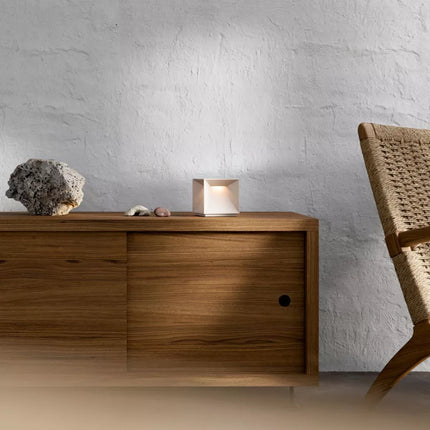 Lampe Nutalis posée sur une console en bois, ambiance chaleureuse avec chaise en fibre tressée.