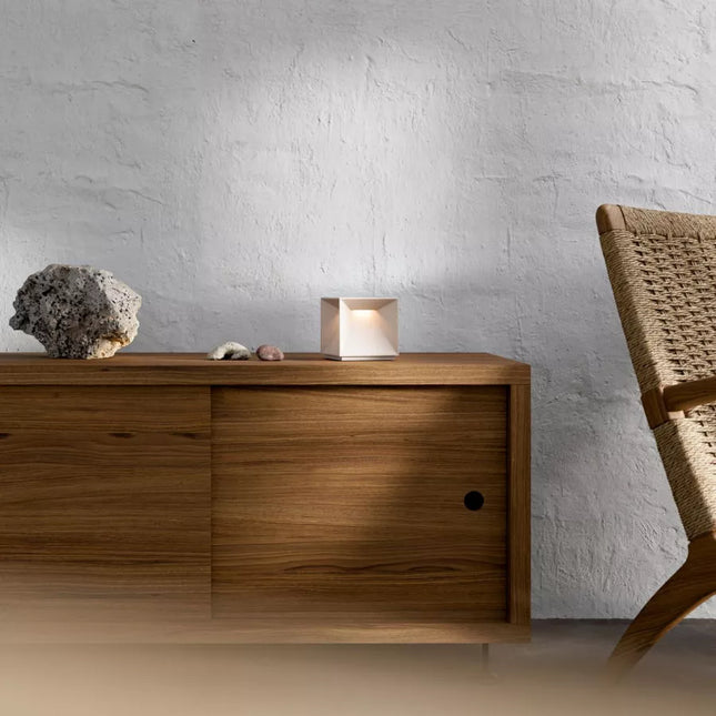 Lampe Nutalis posée sur une console en bois, ambiance chaleureuse avec chaise en fibre tressée.