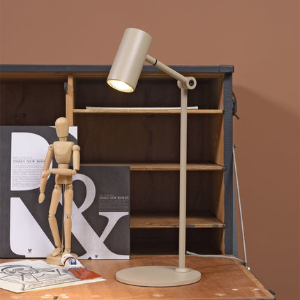 Lampe à poser Montreux sable devant une étagère en bois, lumière chaude allumée