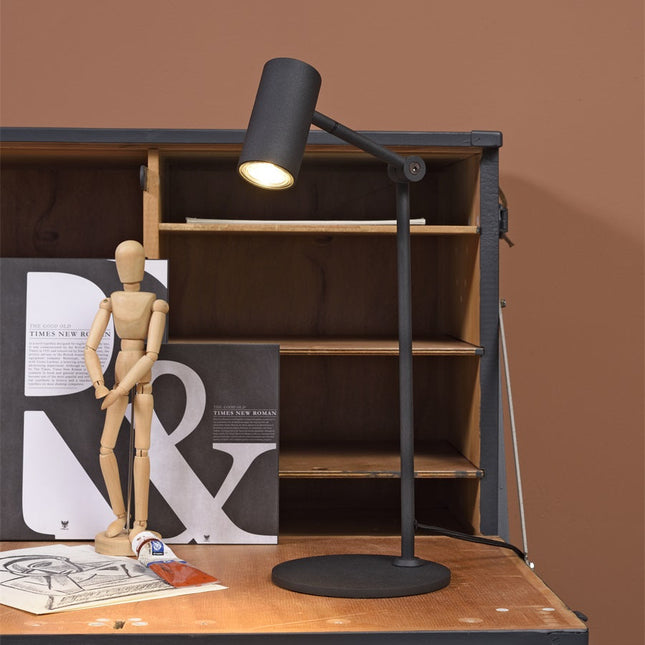 Lampe à poser Montreux noire allumée posée sur un bureau en bois