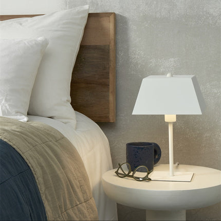 Lampe Perth blanche allumée sur une table de chevet, lumière douce dans une chambre cosy
