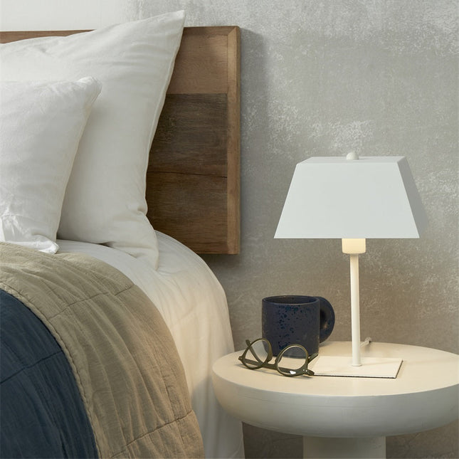 Lampe Perth blanche allumée sur une table de chevet, lumière douce dans une chambre cosy