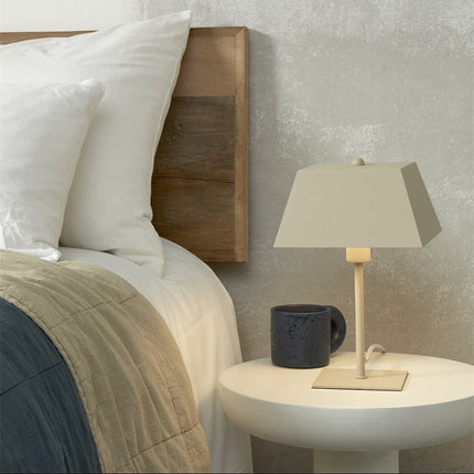 Lampe à poser Perth sable posée sur une table de chevet ronde, à côté d'une tasse en céramique