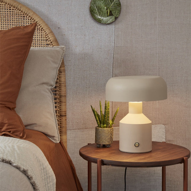 Lampe à poser Porto fer sable allumée sur table de chevet dans une chambre en rotin