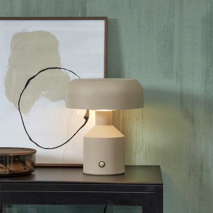 Lampe à poser Porto fer sable allumée sur une console noire devant un tableau