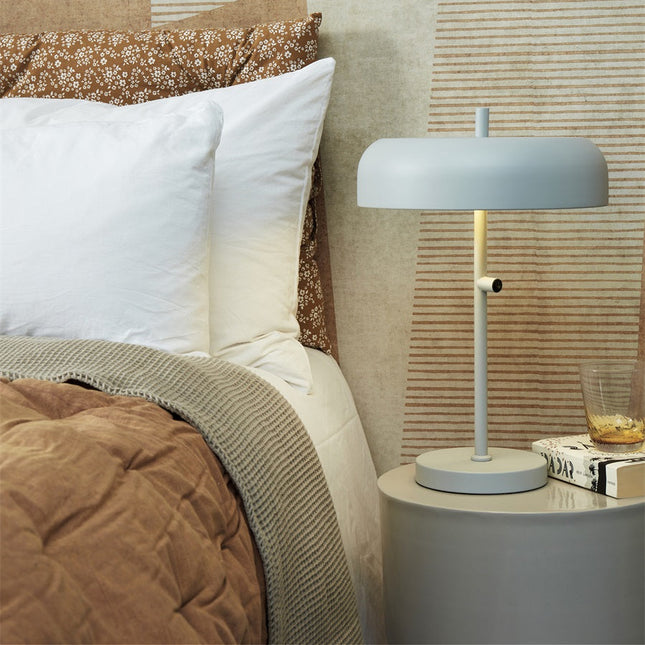 Lampe Porto gris clair posée sur une table de chevet ronde, chambre cosy