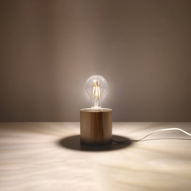 Lampe à poser en bois naturel allumée sur une table, lumière chaude d'ambiance et câble apparent.