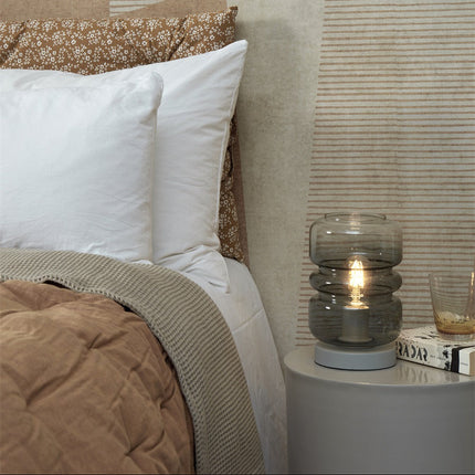 Lampe à poser Verona en verre fumé gris posée sur une table de chevet ronde