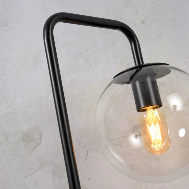 Détail du bras en fer noir plié et du globe en verre transparent de la lampe Warsaw avec ampoule allumée