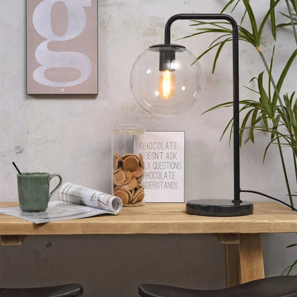 Lampe à poser Warsaw, globe en verre soufflé et structure en fer noir, posée sur un bureau en bois