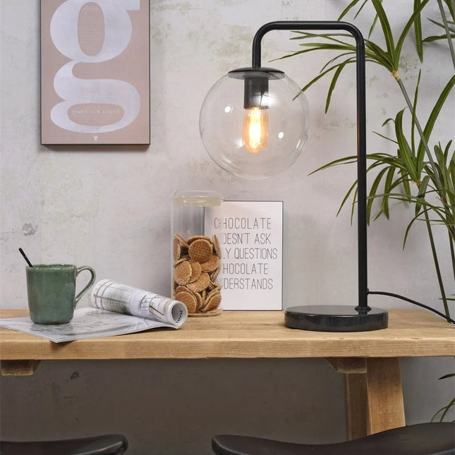 Lampe à poser Warsaw, globe en verre soufflé et structure en fer noir, posée sur un bureau en bois
