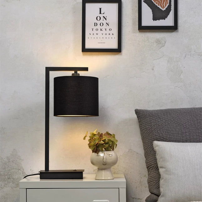 Lampe Boston noire posée sur une table de chevet, lumière chaleureuse diffusée par l'abat-jour en coton.