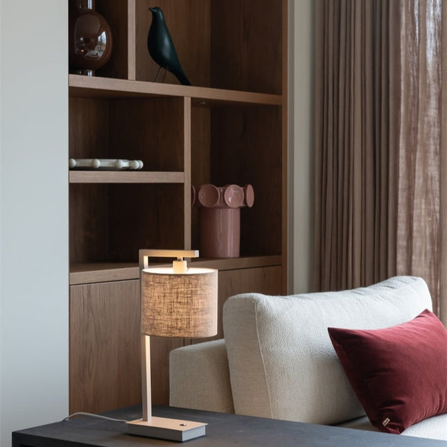 Lampe de table Boston dans un salon, structure sable et abat-jour en coton lin foncé sur meuble bas.