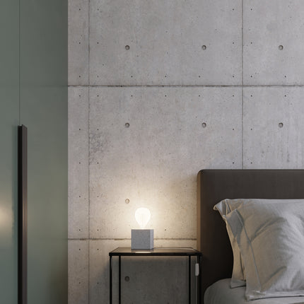 Détail d'une applique Cube en béton allumée sur un mur sombre