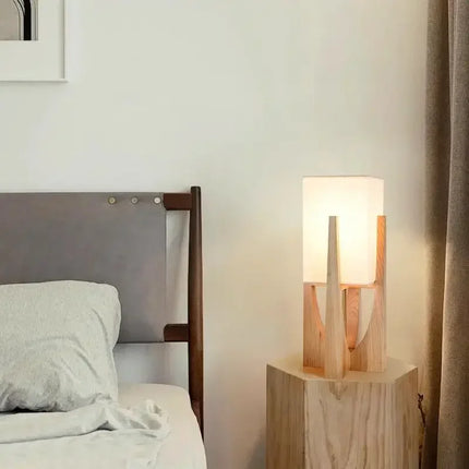 Lampe à poser japonaise en bois clair sur un chevet cube, à côté d'un lit dans une chambre