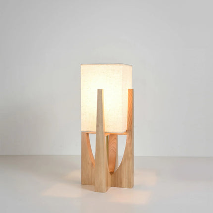 Lampe à poser japonaise en bois clair allumée, abat-jour carré en lin, sur fond neutre