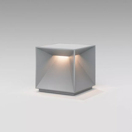 Lampe Nutalis vue de trois quarts, silhouette cubique en aluminium gris brume, lumière chaude diffusée vers le bas