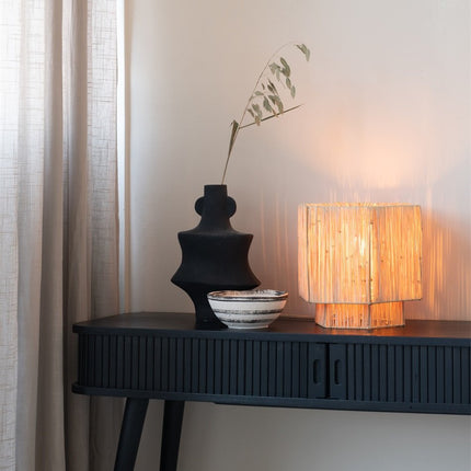 Lampe Panama en raphia naturel allumée, diffusant une lumière chaude et striée dans un salon