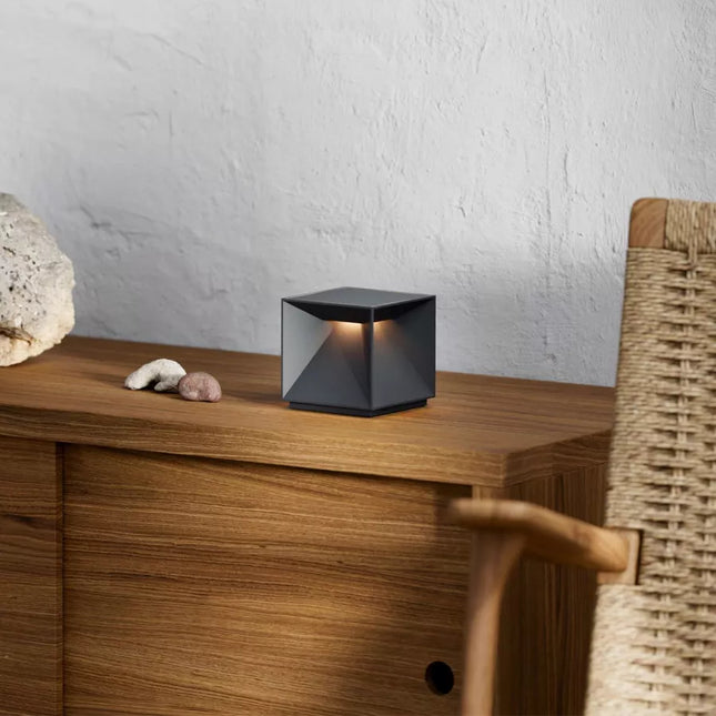 Lampe à poser LED Nutalis noire posée sur un meuble en bois, diffusant une lumière chaude et tamisée