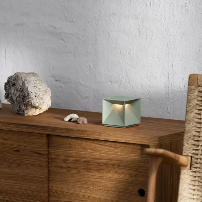Lampe à poser LED Nutalis cube aluminium vert sauge posée sur un meuble en bois, lumière chaude allumée