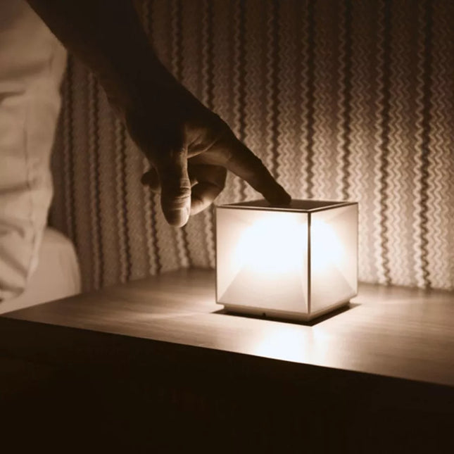 Lampe cube Nutalis allumée sur une table de chevet, lumière chaude diffusée dans la pièce