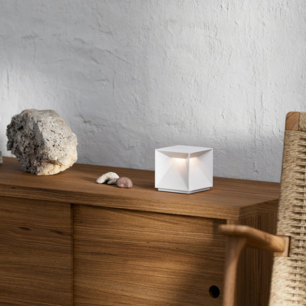 Lampe à poser Nutalis cube aluminium blanc posée sur un meuble bois avec pierres décoratives