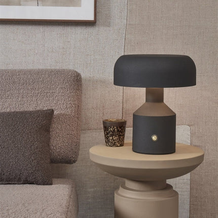 Lampe à poser Porto noire posée sur une table d'appoint dans un salon cosy