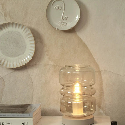 Lampe à poser Verona allumée sur une étagère, entourée de céramiques décoratives