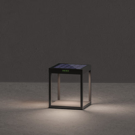Lampe solaire Klewe Radia allumée la nuit, cube en aluminium gris graphite posé sur un sol en béton
