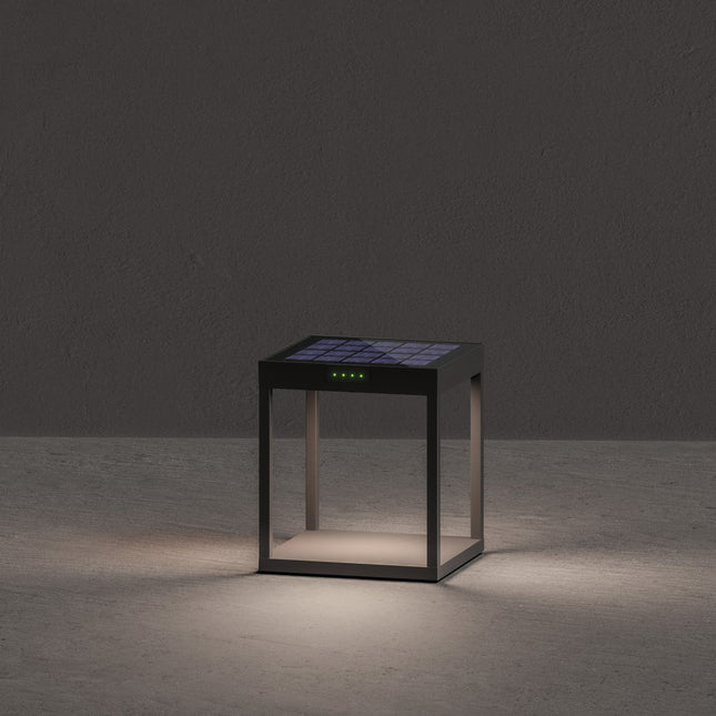 Lampe solaire Klewe Radia allumée la nuit, cube en aluminium gris graphite posé sur un sol en béton