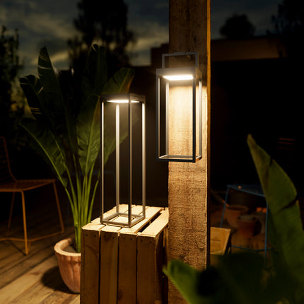 Lampes solaires Numove allumées le soir sur une terrasse, l'une posée sur une caisse en bois, l'autre suspendue au mur