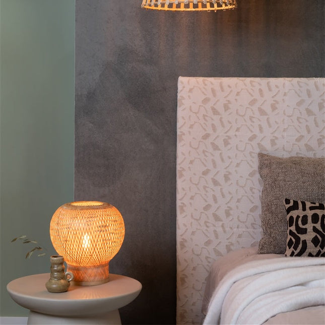 Lampe de table Barbados bambou allumée sur une table de chevet beige, en ambiance de chambre cosy et épurée.